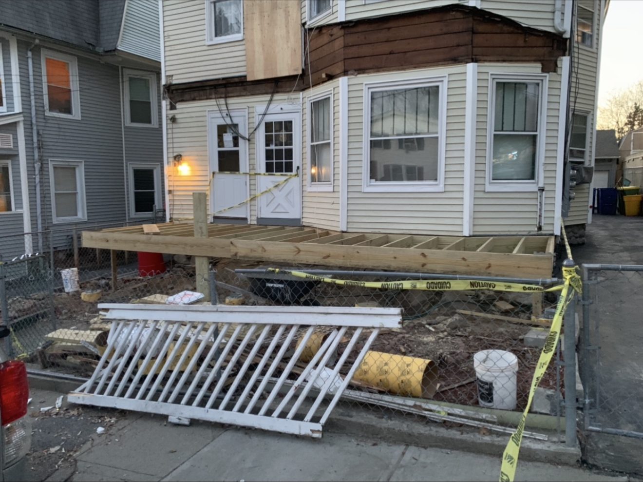Before — bare wood deck framing under construction on a multi-family home, fenced off with caution tape