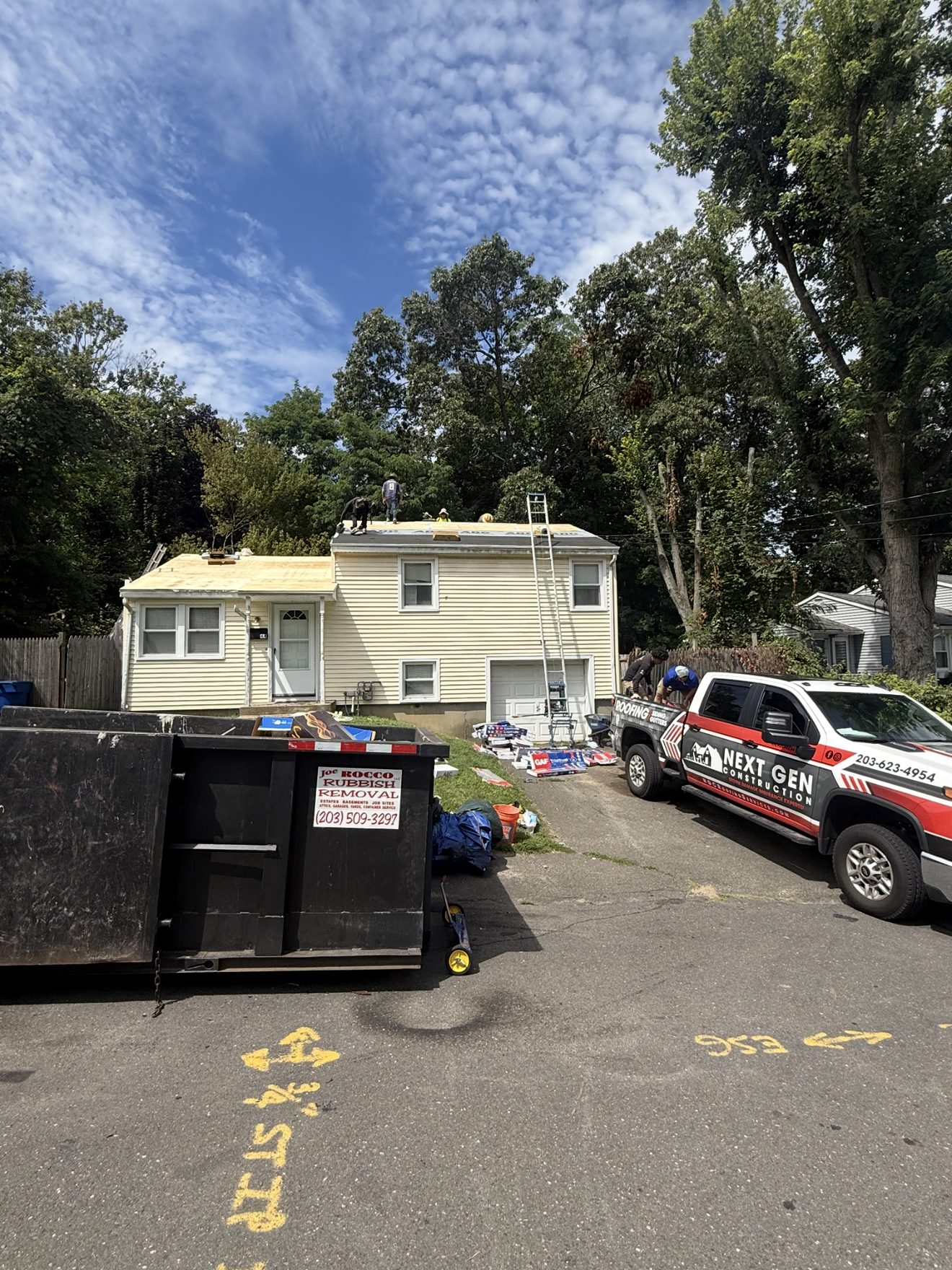 Next Gen Construction crew tearing off a storm-damaged roof and loading a dumpster on an insurance job
